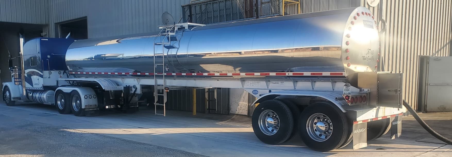 A Wall Transportation power unit coupled to a polished stainless food-grade tank trailer in low evening light.