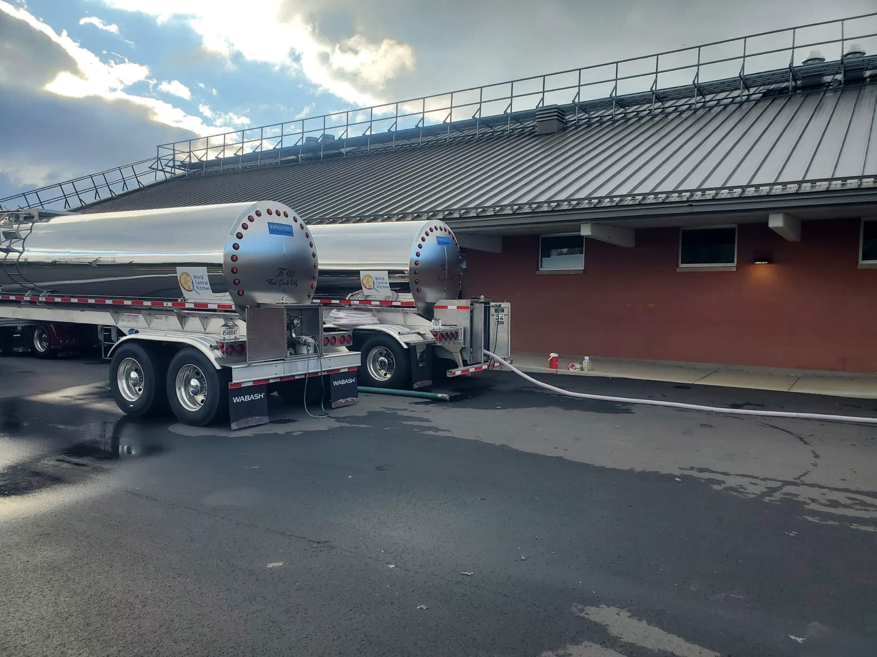 Two Wall Transportation stainless food-grade tankers discharging water through hose lines at a relief site.